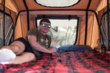 Relaxing inside a spacious **rooftop tent**, part of an **RV rental** adventure. Man smiles, enjoying the **outdoor** comfort.