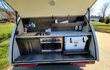 Explore this RV rental's compact outdoor kitchen galley in a teardrop camper, featuring a sink, stove, microwave, and YETI cooler.