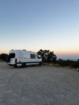 White Sojourn Sprinter **RV rental** parked at sunset, overlooking a scenic valley. Perfect for adventure travel.