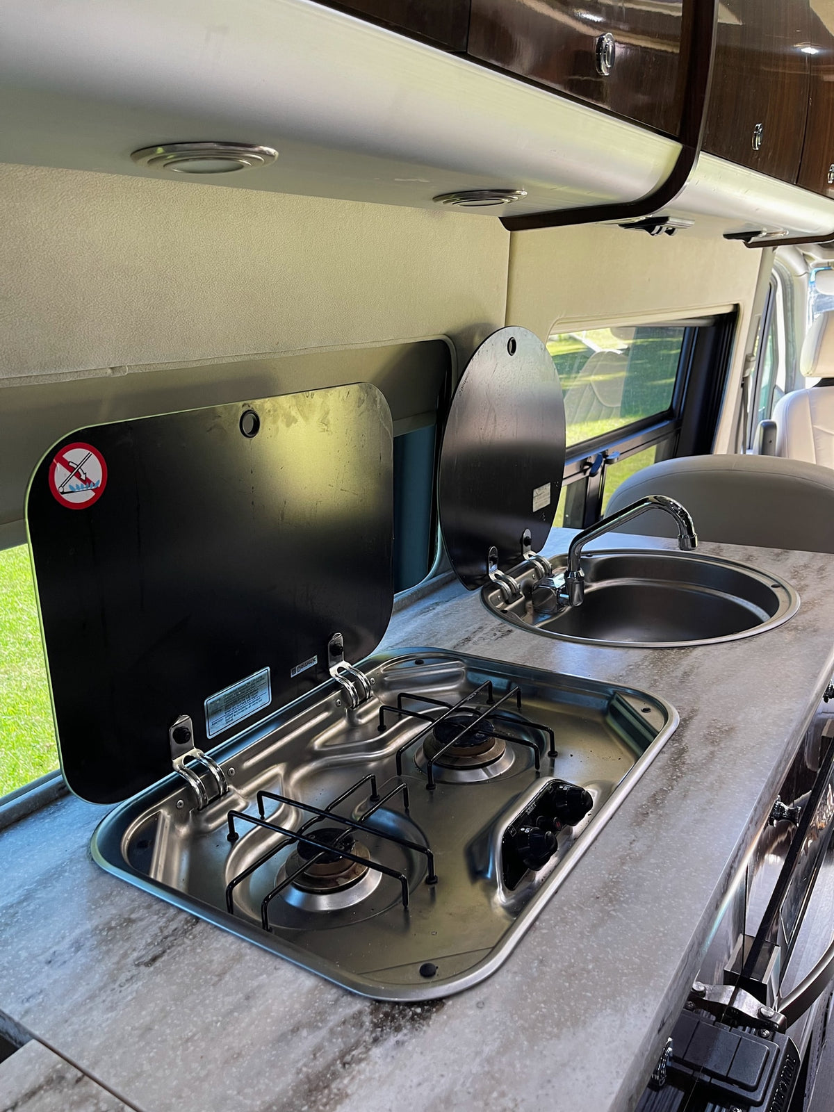 RV rental's compact kitchen setup, featuring a stainless steel two-burner stove, sink, and lifting covers. — photo 11