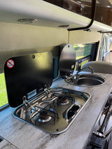 RV rental's compact kitchen setup, featuring a stainless steel two-burner stove, sink, and lifting covers.