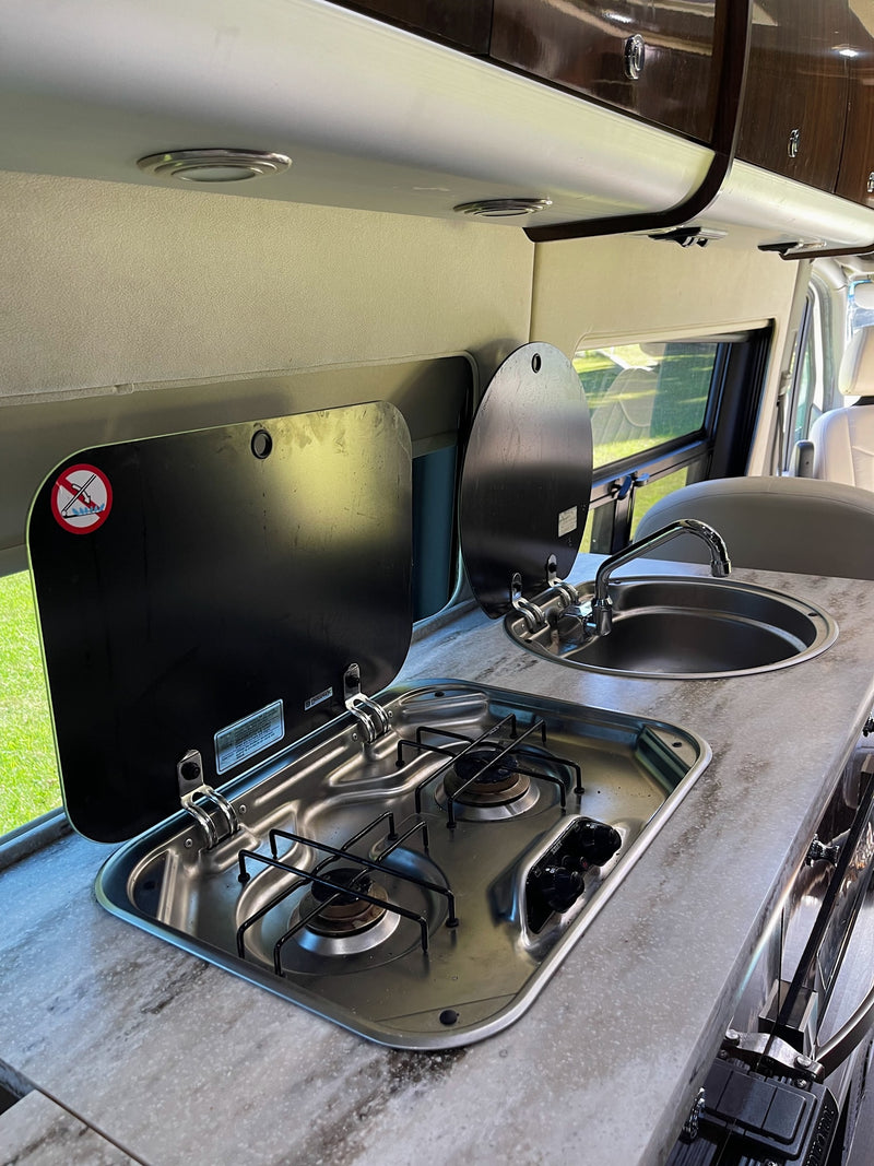 RV rental's compact kitchen setup, featuring a stainless steel two-burner stove, sink, and lifting covers. — photo 11