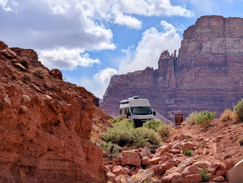 An RV rental is parked on a dirt path, surrounded by towering red rock formations and desert vegetation, with a sign for Cathedral Wash. — photo 8