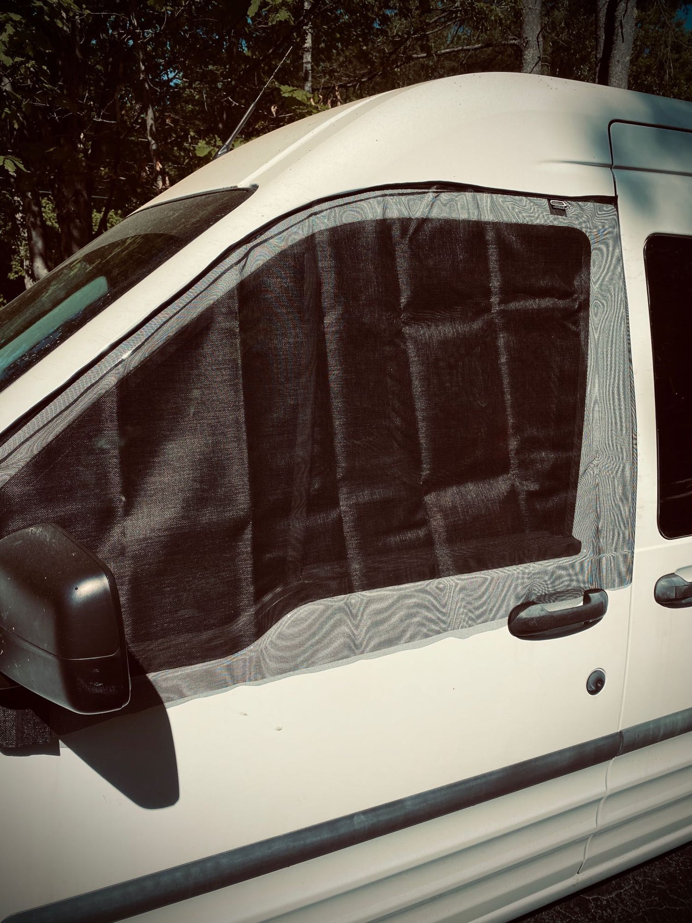 White RV rental van with a black mesh window screen installed on the passenger side for ventilation and bug protection.