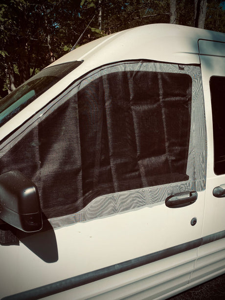 White RV rental van with a black mesh window screen installed on the passenger side for ventilation and bug protection.