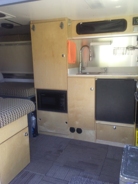 Explore this efficient rv rental interior: a light wood kitchen with sink and fridge, plus a cozy patterned living space.