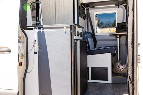 RV rental interior with a functional kitchenette, control panel, seating, and a small dog in a cozy bed. Your mobile home!