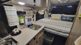 Cozy RV rental interior with compact kitchen & sink next to a comfortable bed for travel.