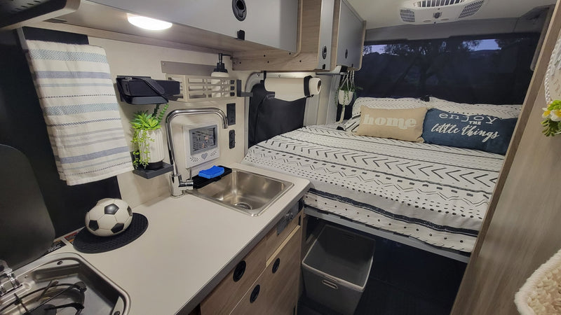 Cozy RV rental interior with compact kitchen & sink next to a comfortable bed for travel. — photo 5