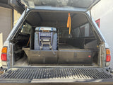 Straight-on view from the open tailgate showing the closed Extendobed drawer fronts with the Extendobed badge and the ARB fridge strapped on its slide