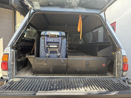 Straight-on view from the open tailgate showing the closed Extendobed drawer fronts with the Extendobed badge and the ARB fridge strapped on its slide