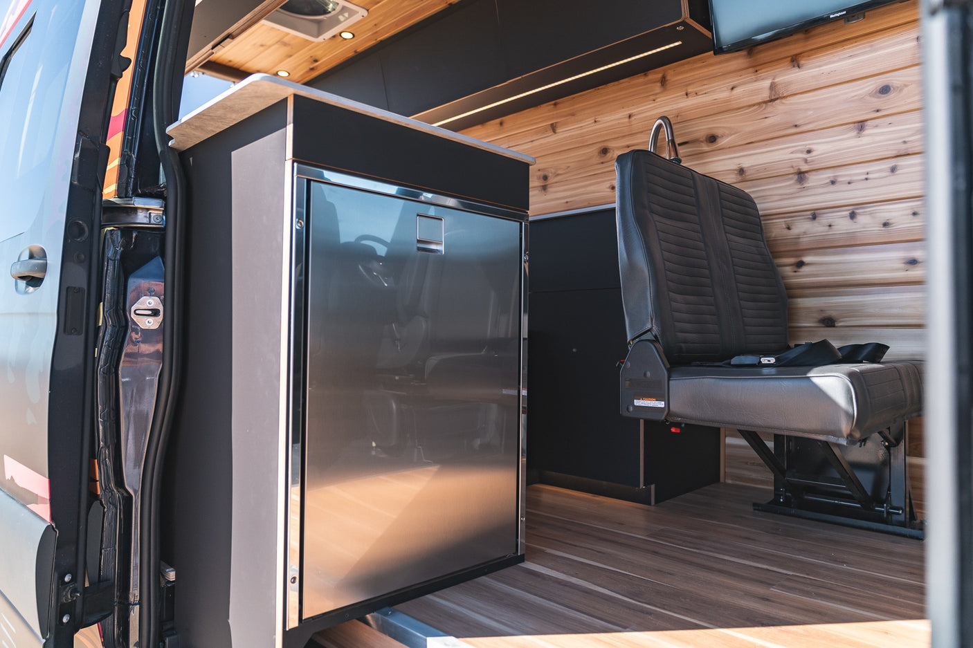 View inside an **RV rental** shows a shiny fridge, a dark passenger seat, and warm wooden walls & floor.