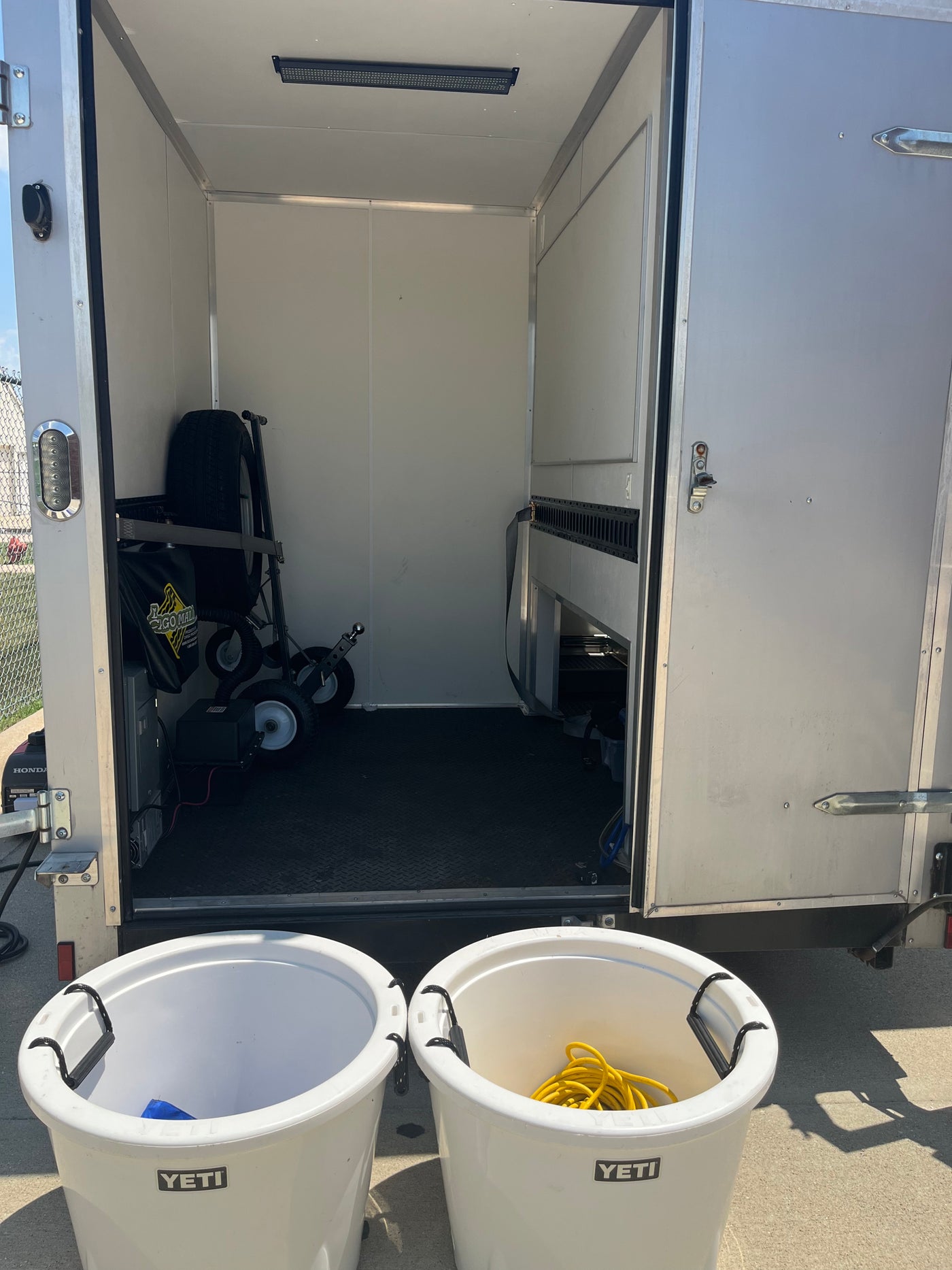 RV rental mobile trailer with generator, equipment, and wall-mounted E-track inside. Two YETI buckets at the entrance. — photo 6
