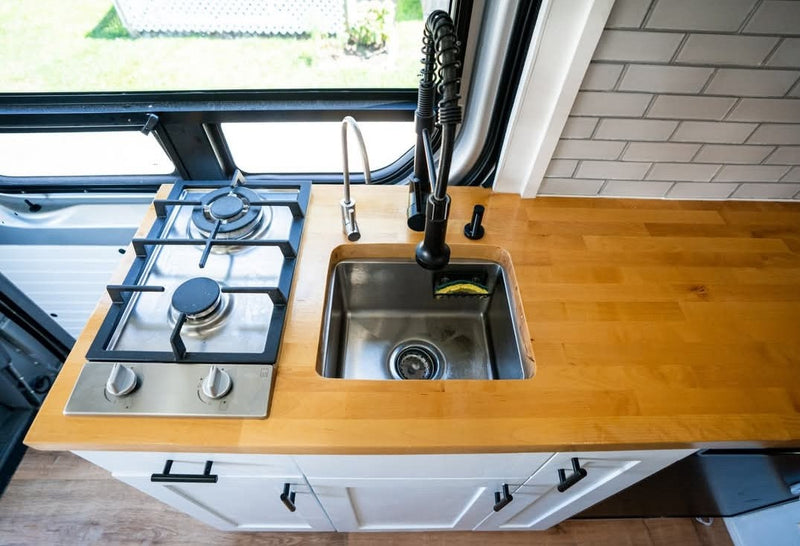 Modern rv rental kitchen with a two-burner stove, stainless sink, dual faucets, and wood counter. Perfect for travel cooking. — photo 15