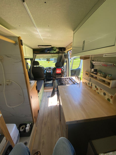 Explore this bright rv rental camper van interior, featuring a full kitchen, shower, and cozy living space looking out to nature.