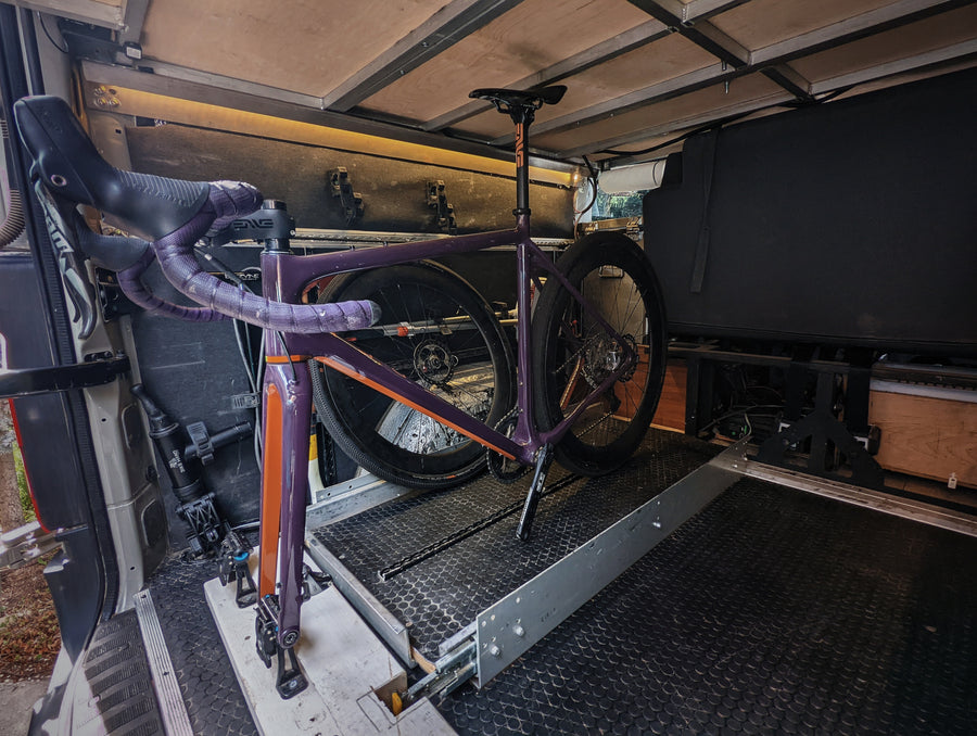 Inside an RV rental, a purple gravel bike is securely mounted on a slide-out tray, optimizing space for travel.