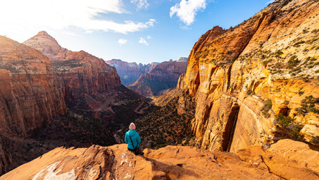 Breathtaking canyon vistas await your RV rental journey! A person sits on a cliff, gazing at vast red rock mountains & valleys.