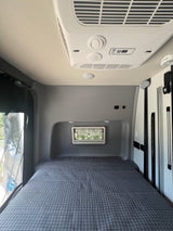 Inside an rv rental, a cozy campervan bedroom features a blue patterned bed, AC unit, and small window for views.
