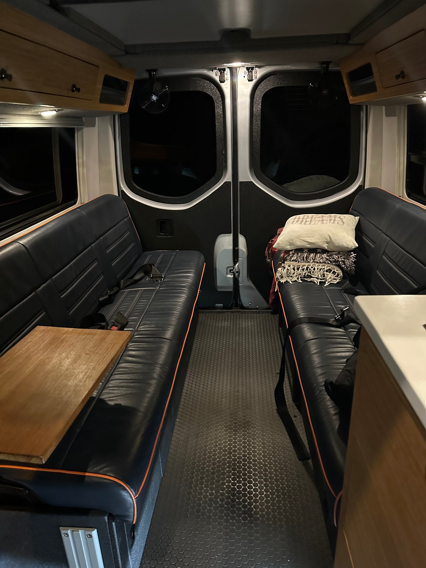 RV rental interior: dark benches with wood table, textured floor, rear windows. Overhead storage completes this mobile space.