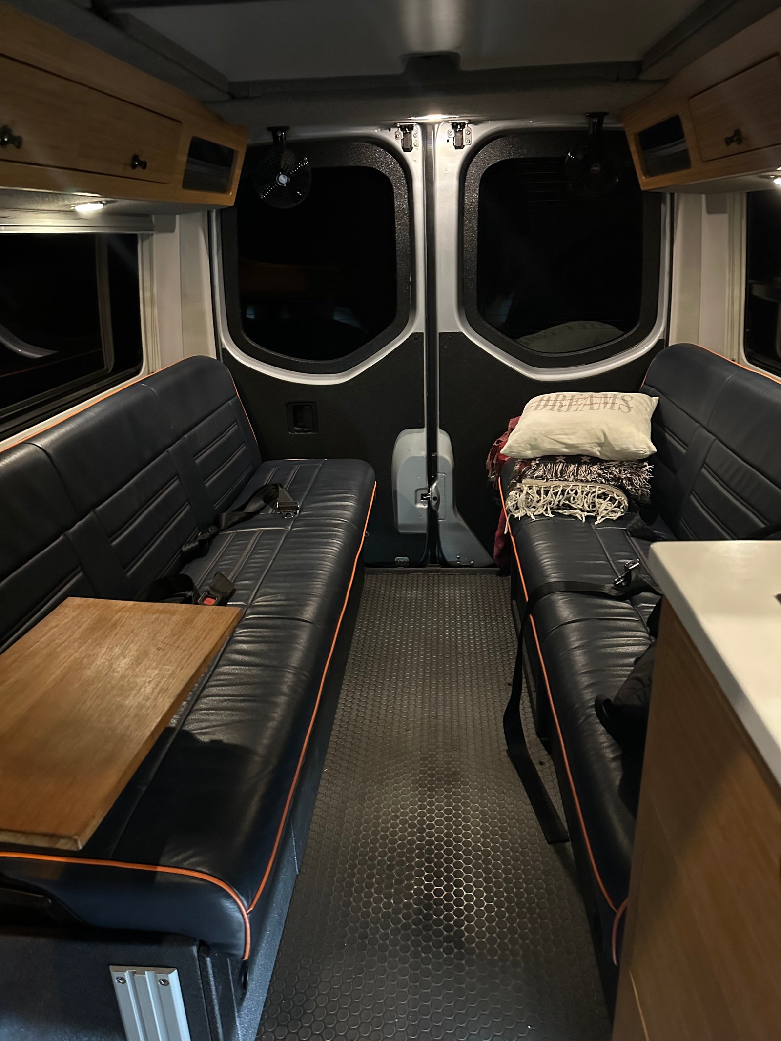 RV rental interior: dark benches with wood table, textured floor, rear windows. Overhead storage completes this mobile space.