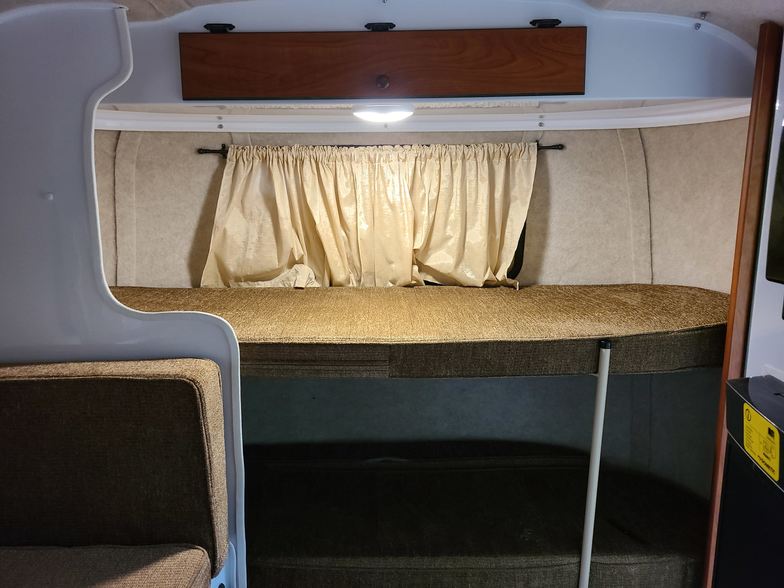 Cozy RV rental interior with bunk beds, curtains, and overhead storage, designed for compact living.
