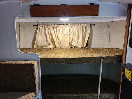 Cozy RV rental interior with bunk beds, curtains, and overhead storage, designed for compact living.