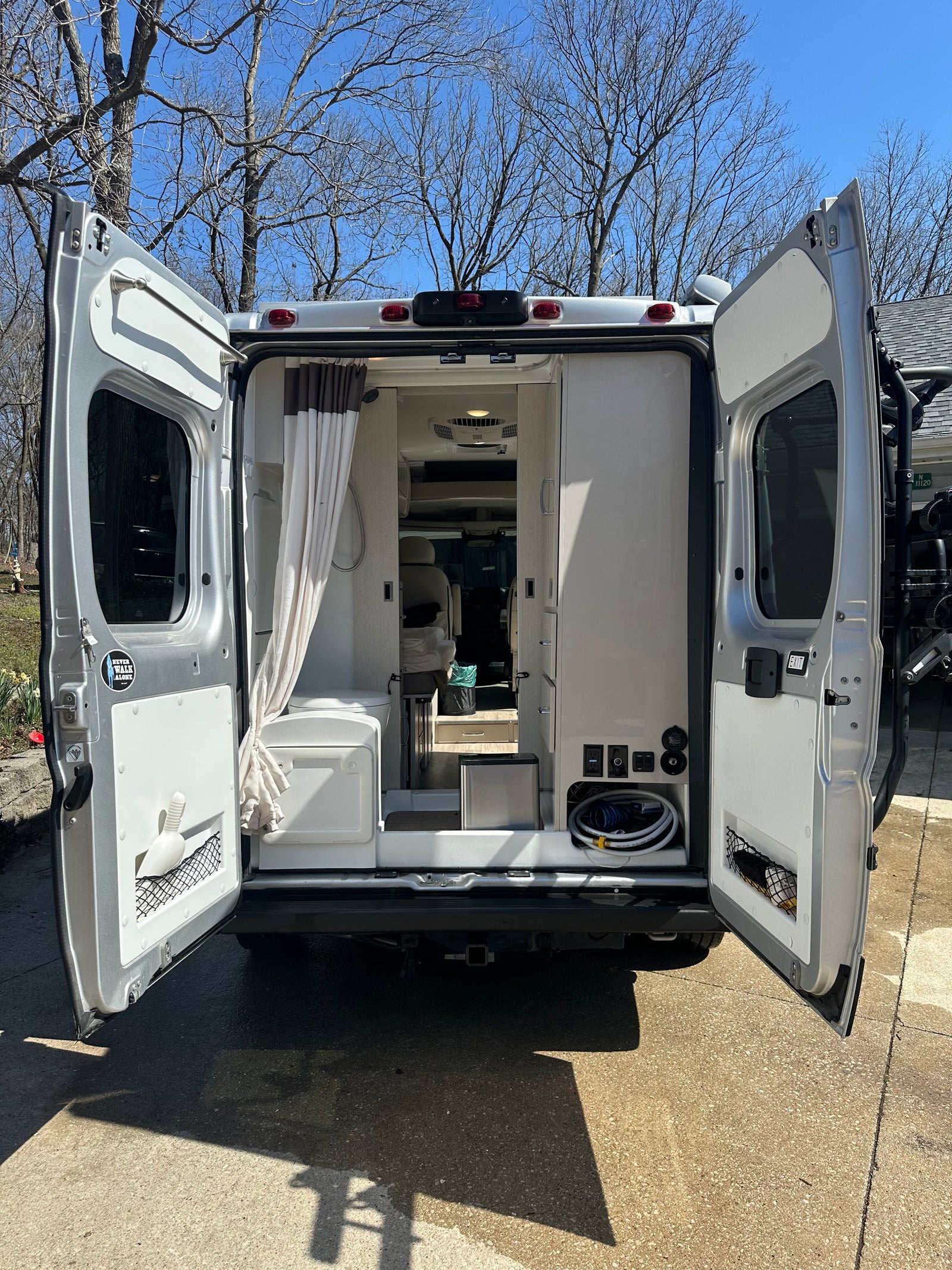 Rear view of an RV rental camper van with open doors, revealing its compact interior including a shower and utility hookups.
