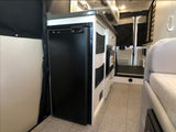 Compact RV rental interior featuring a built-in fridge, kitchenette, and hallway leading to the rear. Ideal for mobile living.