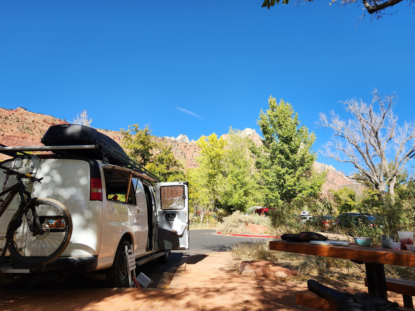 Adventure-ready RV rental: white van with bike rack at scenic red rock campsite with autumn trees. — photo 5