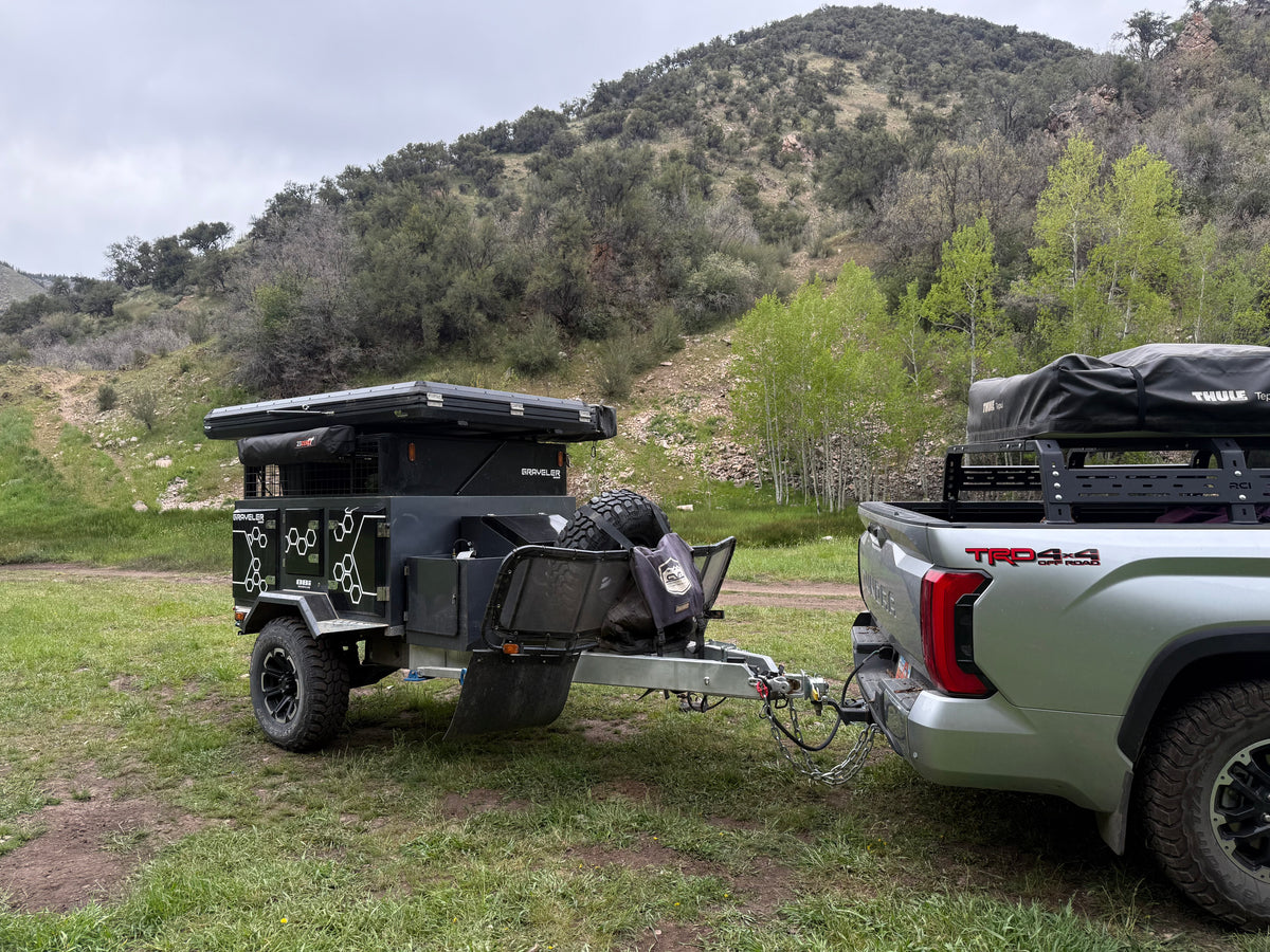 An overland RV rental trailer with rooftop tent hitched to a truck, parked in a grassy mountain area. — photo 2