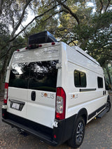 This white Winnebago Solis camper van, ideal for rv rental, is parked beneath large trees, ready for adventure.