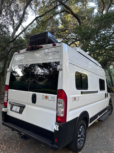 This white Winnebago Solis camper van, ideal for rv rental, is parked beneath large trees, ready for adventure.