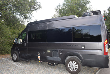 A gray Thor Sequence RV rental (campervan) is parked on gravel beside trees, ready for your next adventure.