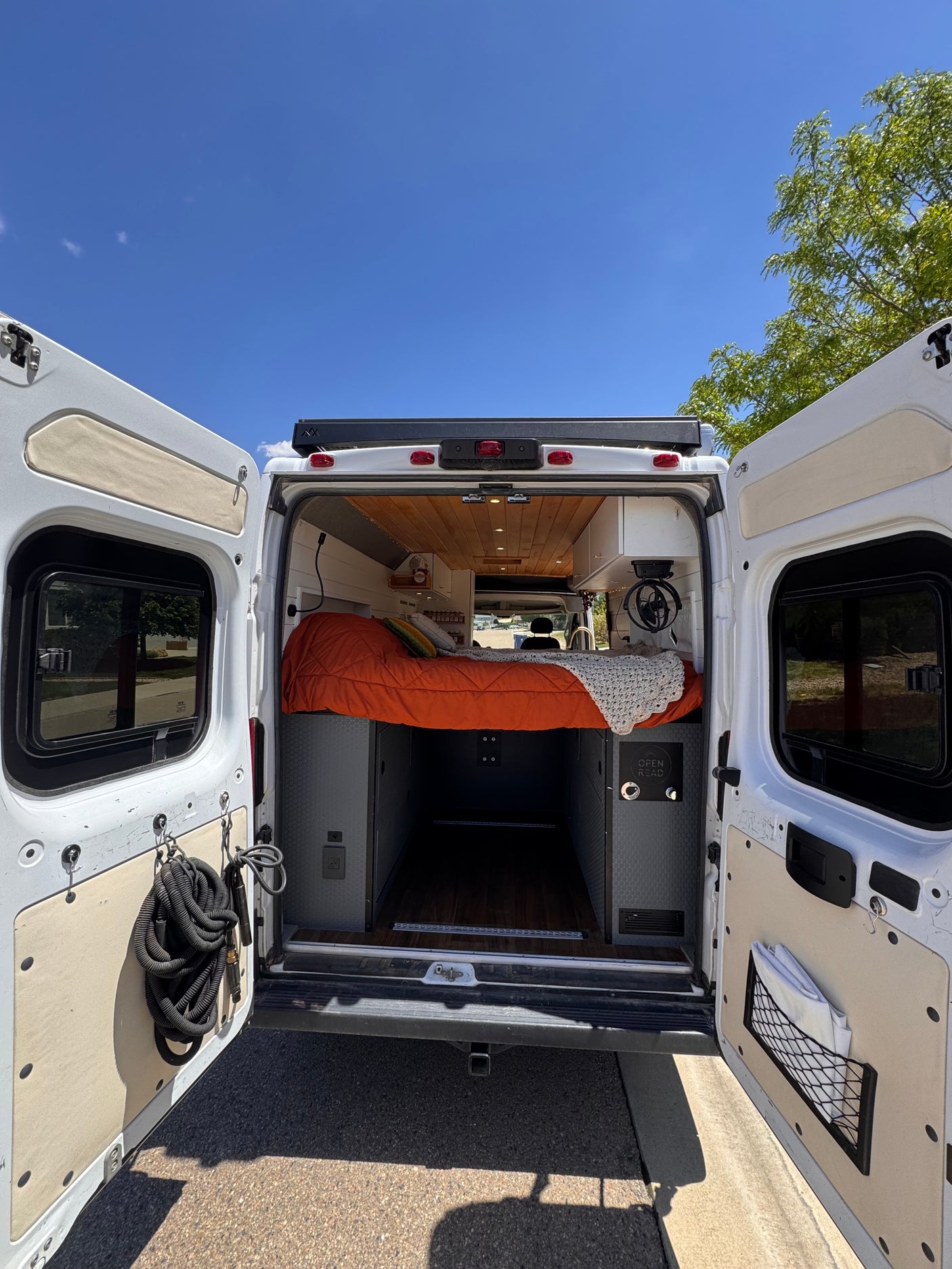 Explore this rv rental's organized interior: open rear doors reveal a cozy bed, ample storage, and wooden ceiling.