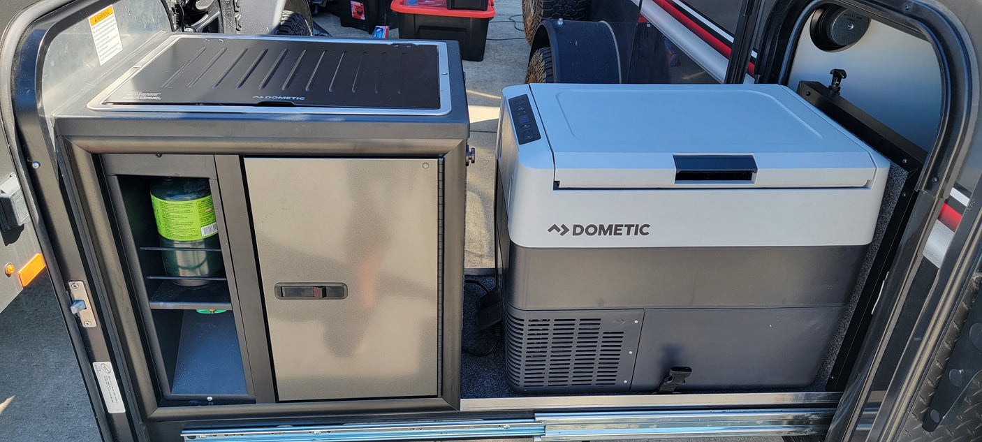 RV rental outdoor kitchen with Dometic cooktop, propane tank, and portable fridge on a pull-out slide for easy access.