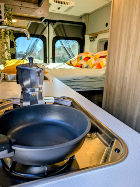 Enjoy morning coffee and cooking in your cozy rv rental kitchen, featuring a Moka pot, pan, and a view to the comfortable bed.