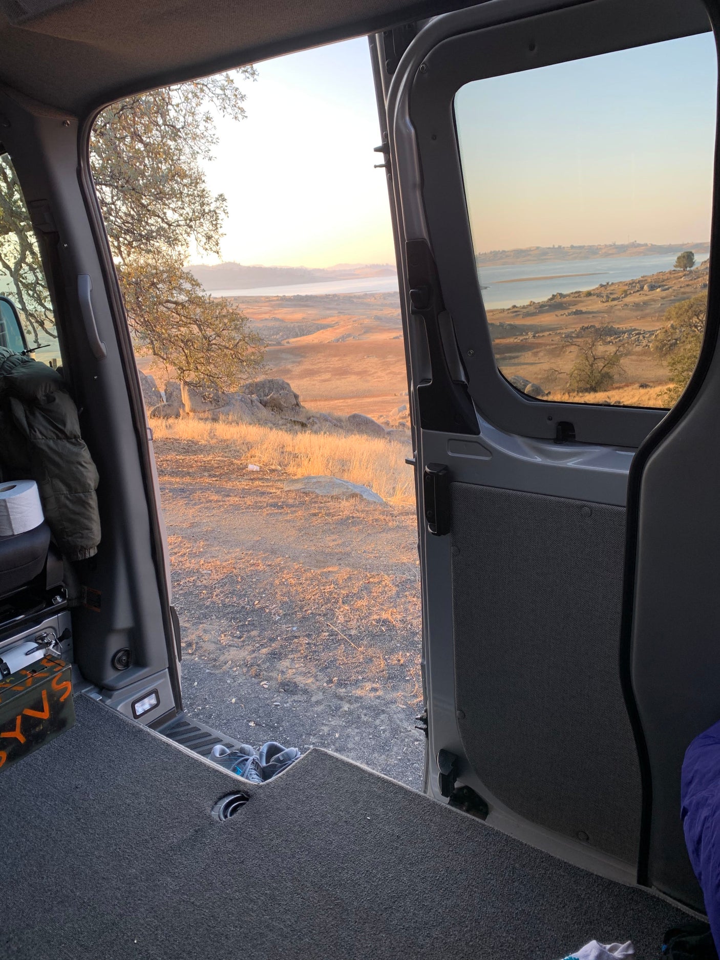 RV rental: Enjoy the stunning sunrise over a lake and hills from inside a cozy camper van.