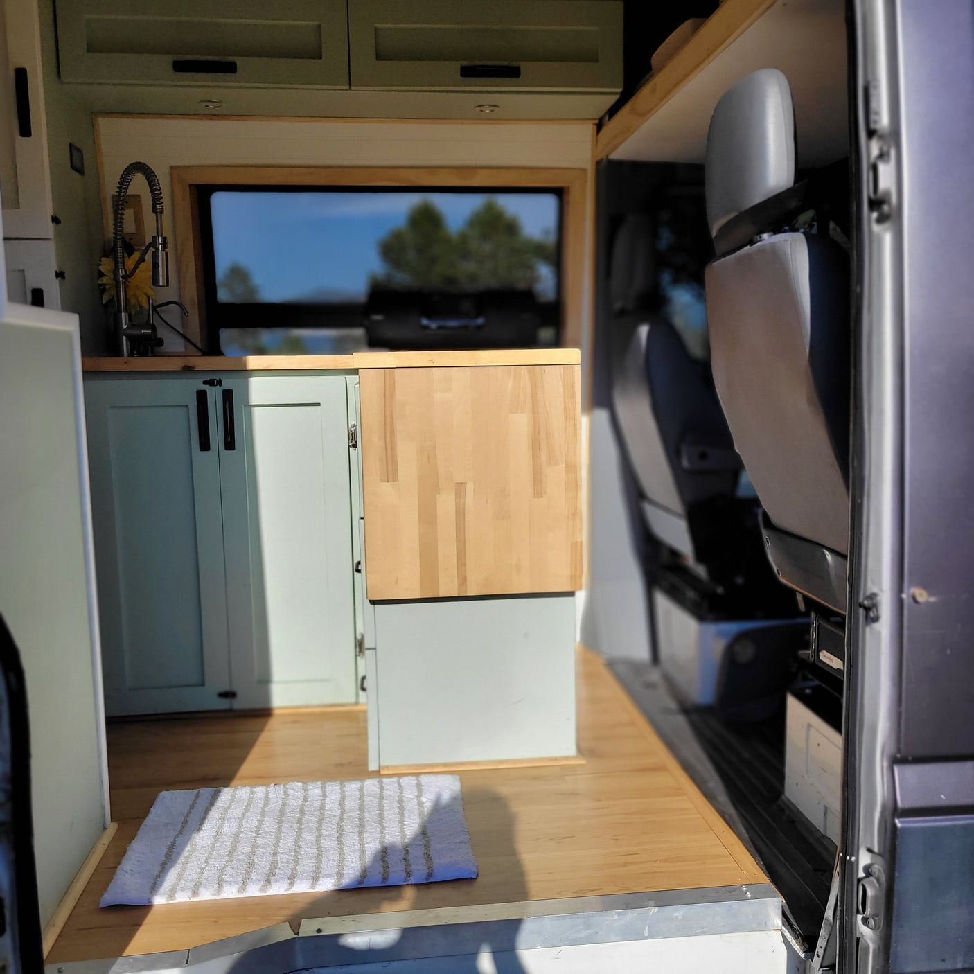 Cozy camper van RV rental interior with light green kitchen, wood counter & floor. Ready for mobile adventures!