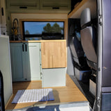 Cozy camper van RV rental interior with light green kitchen, wood counter & floor. Ready for mobile adventures!