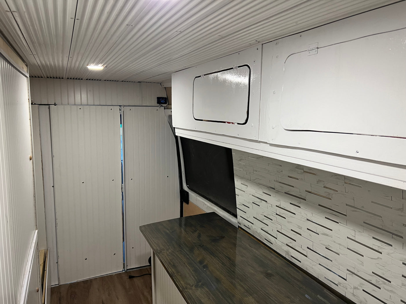 RV rental: Camper van interior featuring white corrugated ceiling, panelled walls, overhead cabinets, dark counter, and tiled backsplash. — photo 3