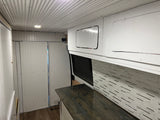 RV rental: Camper van interior featuring white corrugated ceiling, panelled walls, overhead cabinets, dark counter, and tiled backsplash.