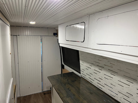 RV rental: Camper van interior featuring white corrugated ceiling, panelled walls, overhead cabinets, dark counter, and tiled backsplash.