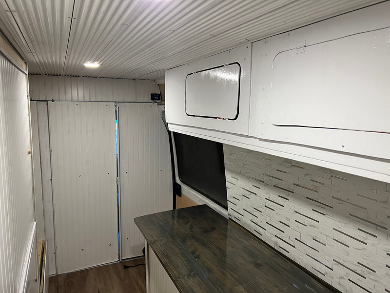 RV rental: Camper van interior featuring white corrugated ceiling, panelled walls, overhead cabinets, dark counter, and tiled backsplash. — photo 3