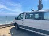 White van, perfect for an RV rental, parked ocean-side. People inside, utility pole nearby. Scenic coastal view.