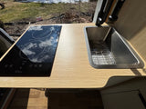 RV rental kitchen features a sleek induction cooktop and stainless steel sink set in a light wood counter.