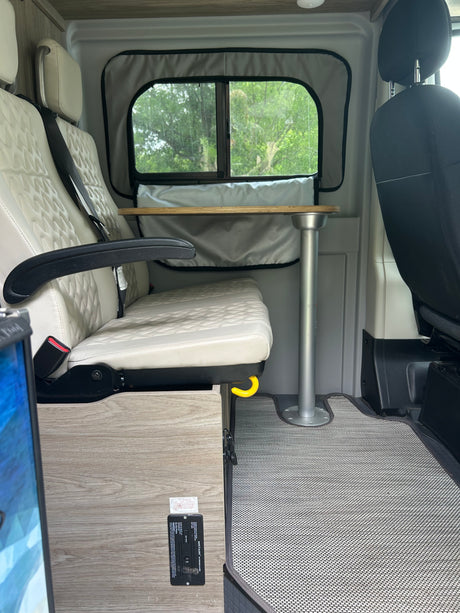 RV rental interior: Cream quilted seats, a removable table, and a vital SAFE-T-ALERT propane alarm for safety.