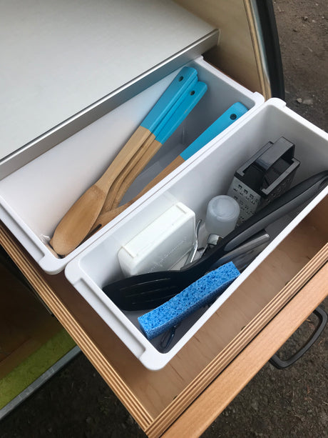 Close-up of an organized RV rental kitchen drawer containing wooden utensils, grater, and cleaning sponge.