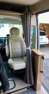 Interior of an RV rental featuring a plush tan seat, drawn gray curtain, and sleek wood-grain floor. Outside is a garage.