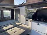 Inside an RV rental: view of the kitchenette, convertible sleeping area, and pop-top for extra space.