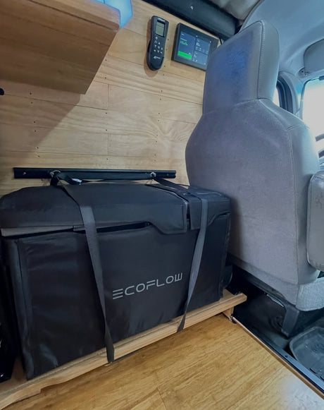 An EcoFlow portable fridge-freezer is neatly secured on a wooden platform inside an RV rental, offering efficient storage.